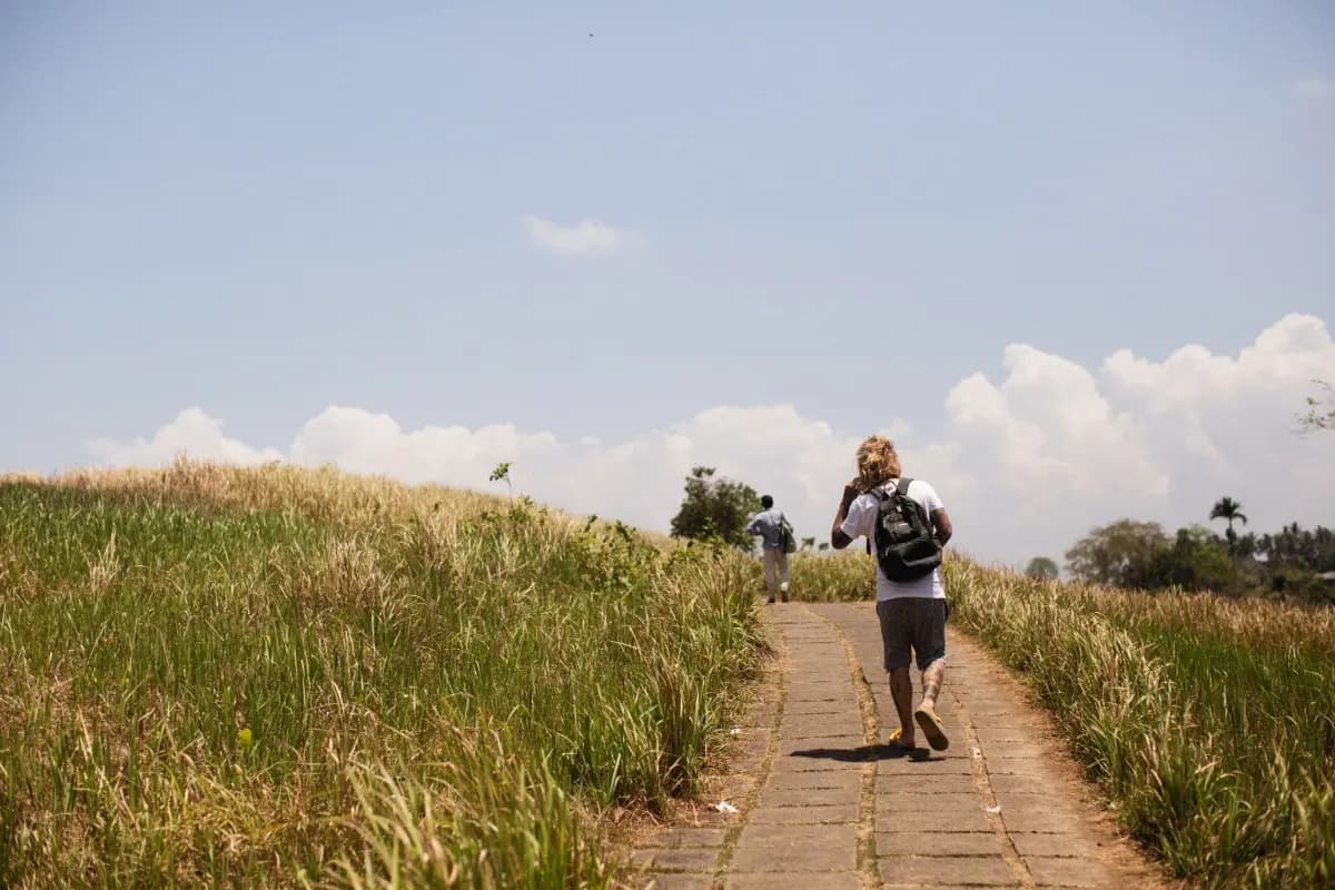 Traveler walks along the Campuhan Ridge Walk path, surrounded by open grass and peaceful Ubud scenery.