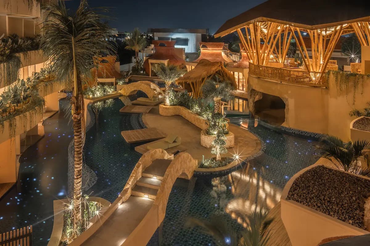 Lagoon-style pool at La Mewali Resort & Spa Canggu illuminated at night with bridges and tropical landscaping.