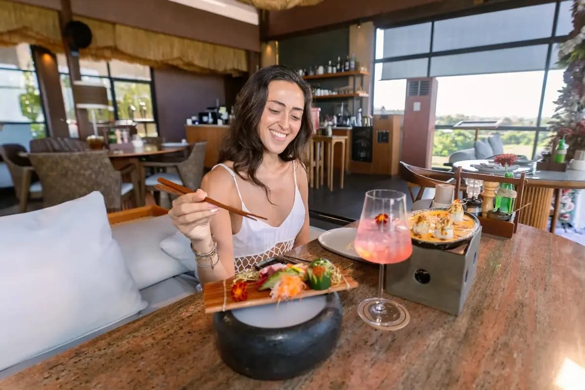 A woman enjoys sushi and drinks at a restaurant, showing a relaxed dinner experience in Sanur.