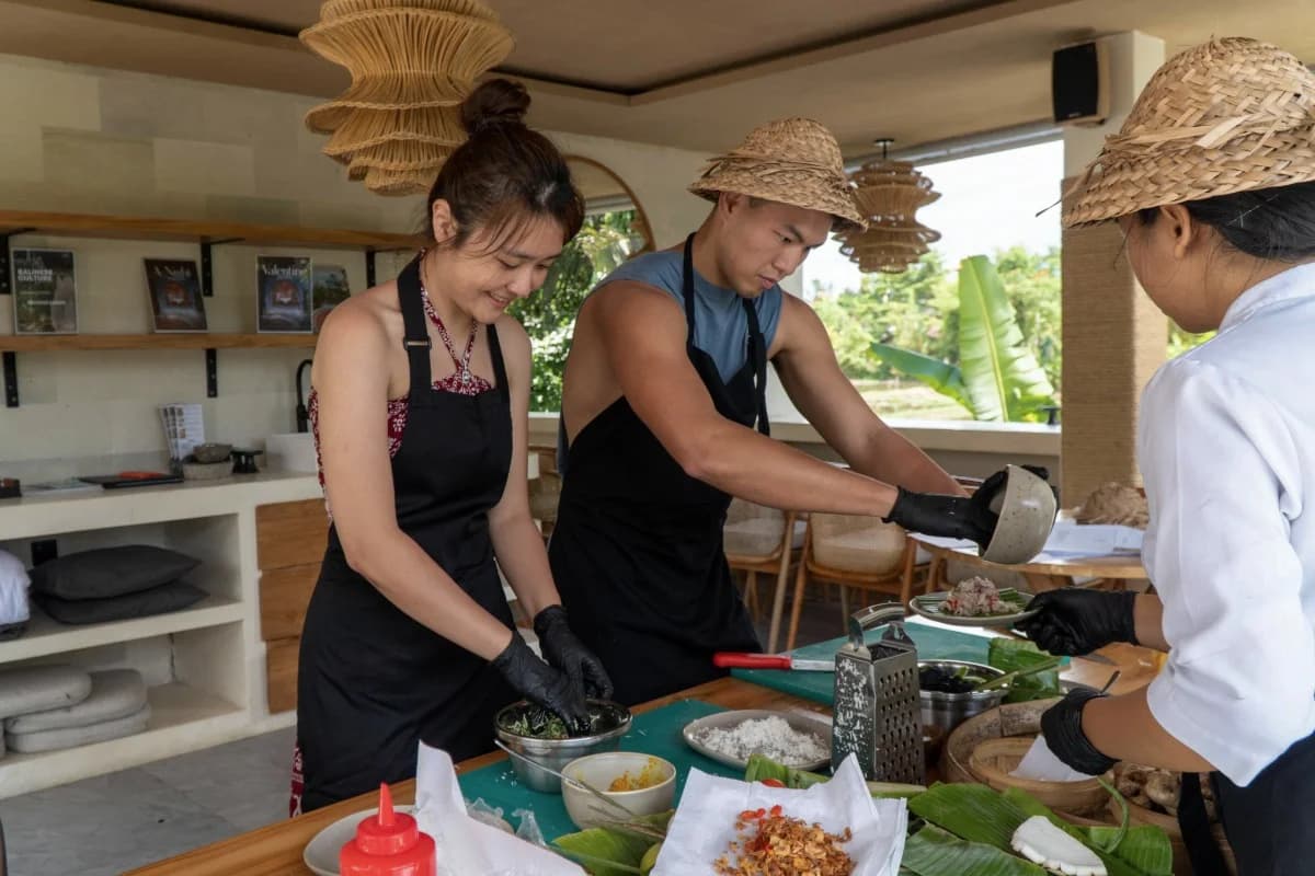 Travelers wearing aprons prepare traditional Balinese dishes together during a hands-on cooking class in Bali.