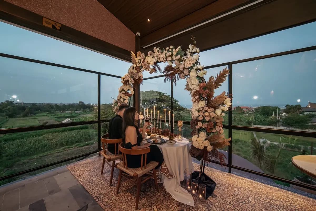 A couple enjoys a birthday dinner in Bali with candles, flowers, and wide evening views from the restaurant.