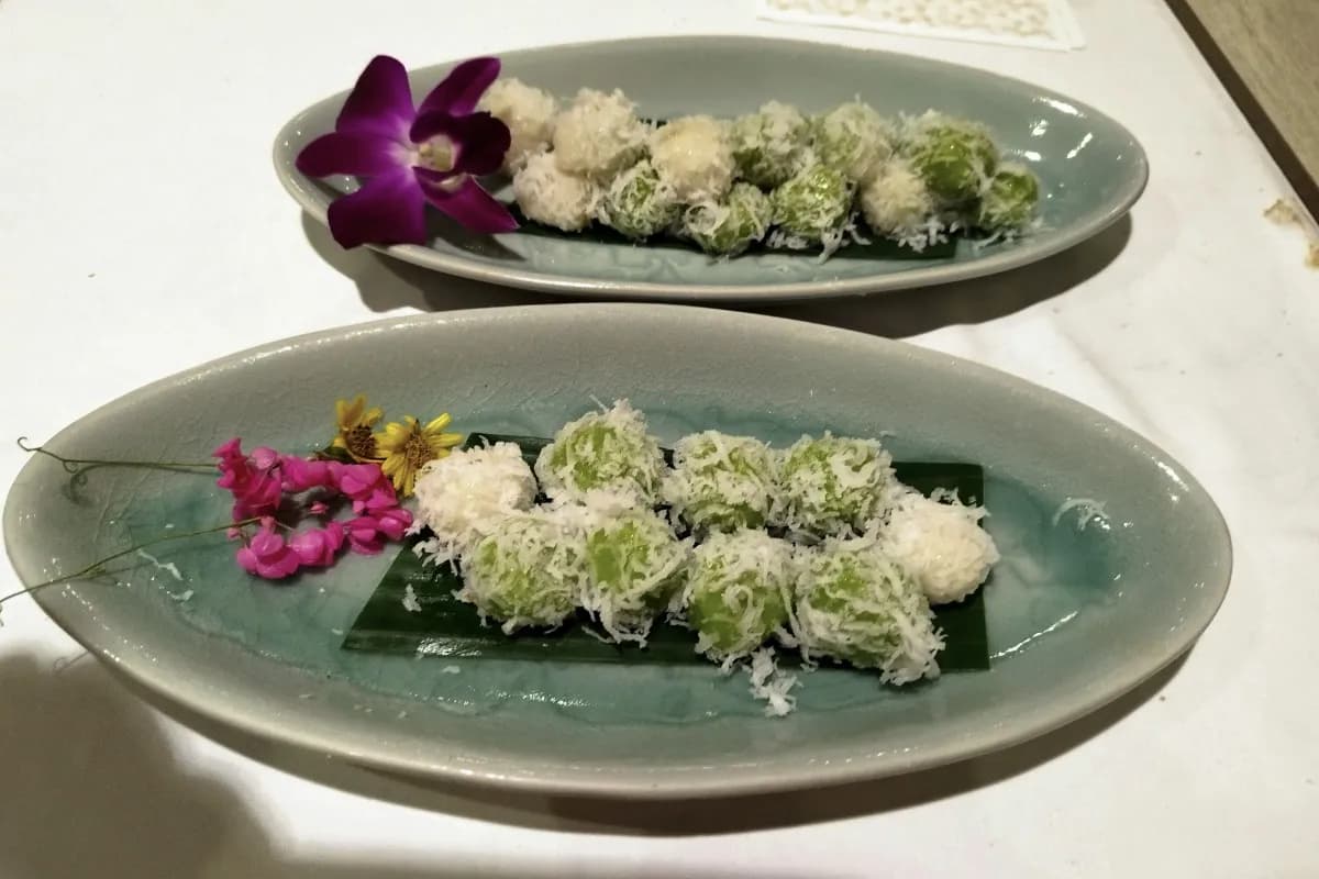 Traditional Balinese jaje served on banana leaves, with green and white coconut-covered sweets decorated with flowers.