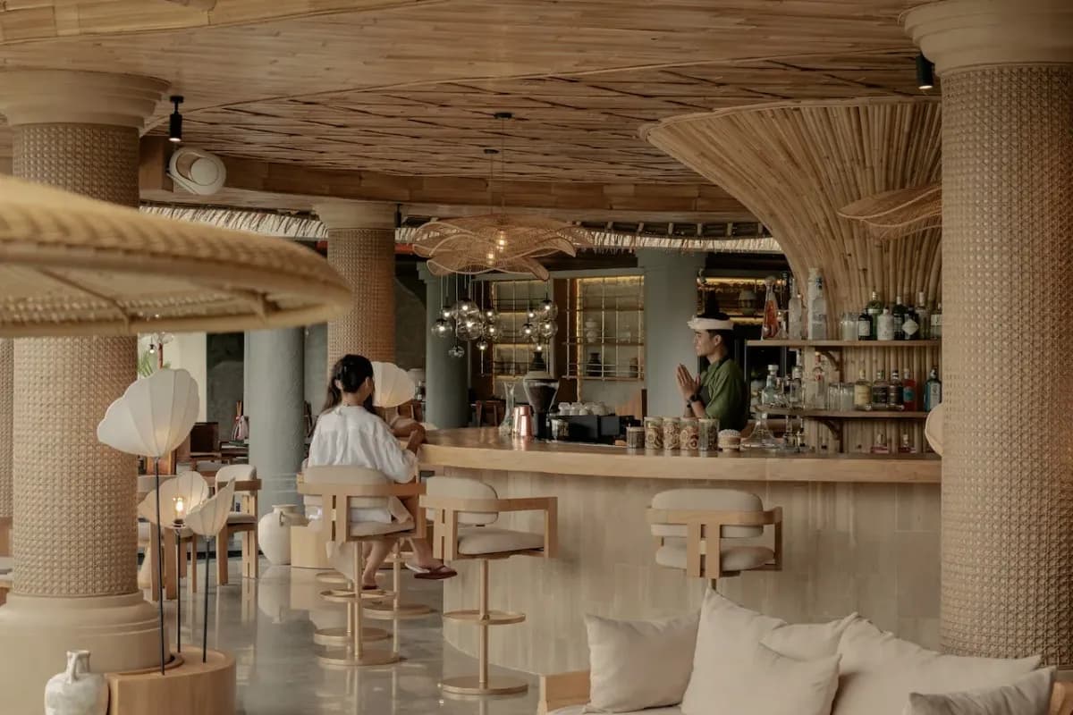 A stylish Ubud lounge with a bar counter, woven decor, comfortable seating, and a guest enjoying a drink.