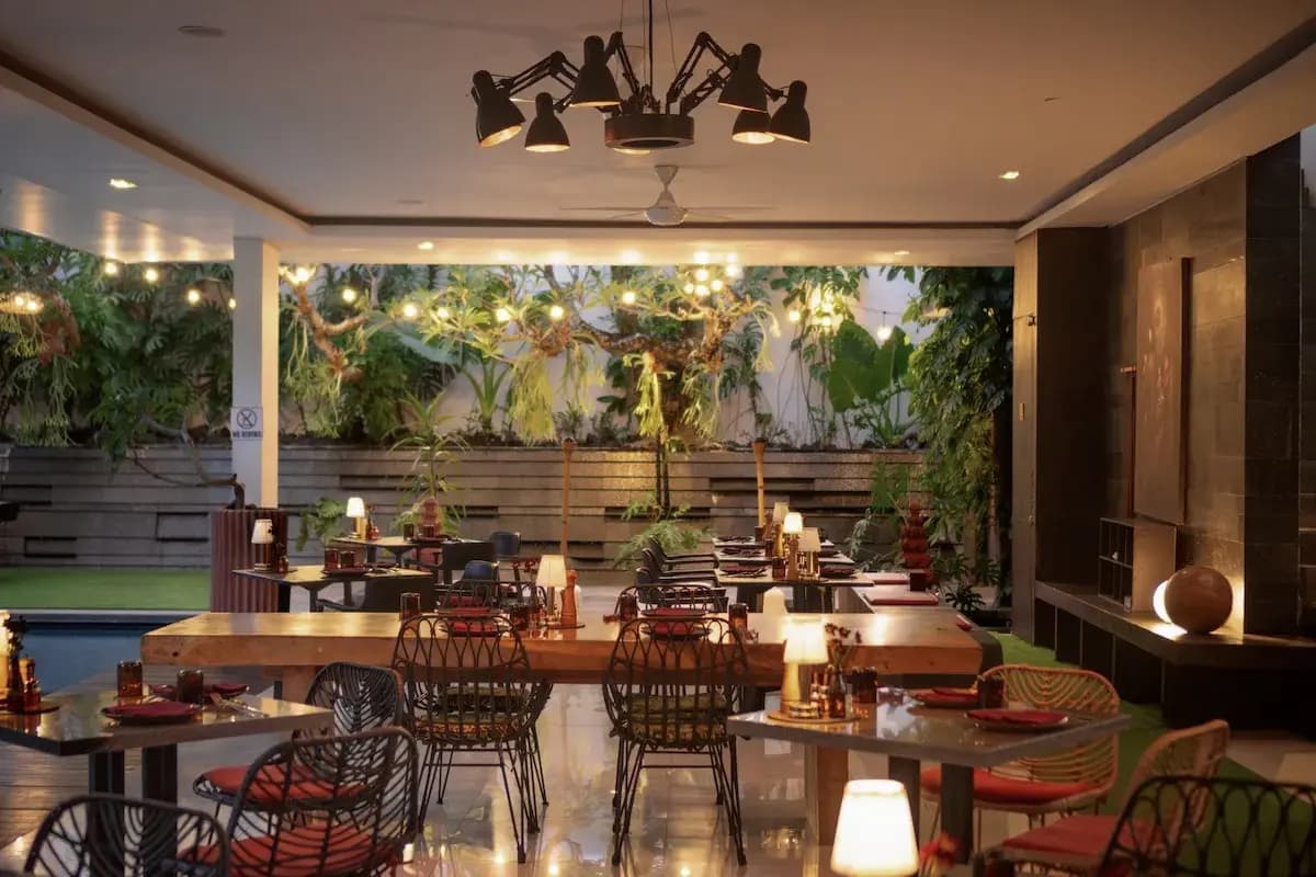 A cozy restaurant interior in Umalas with wooden tables, woven chairs, warm lighting, and a garden view.
