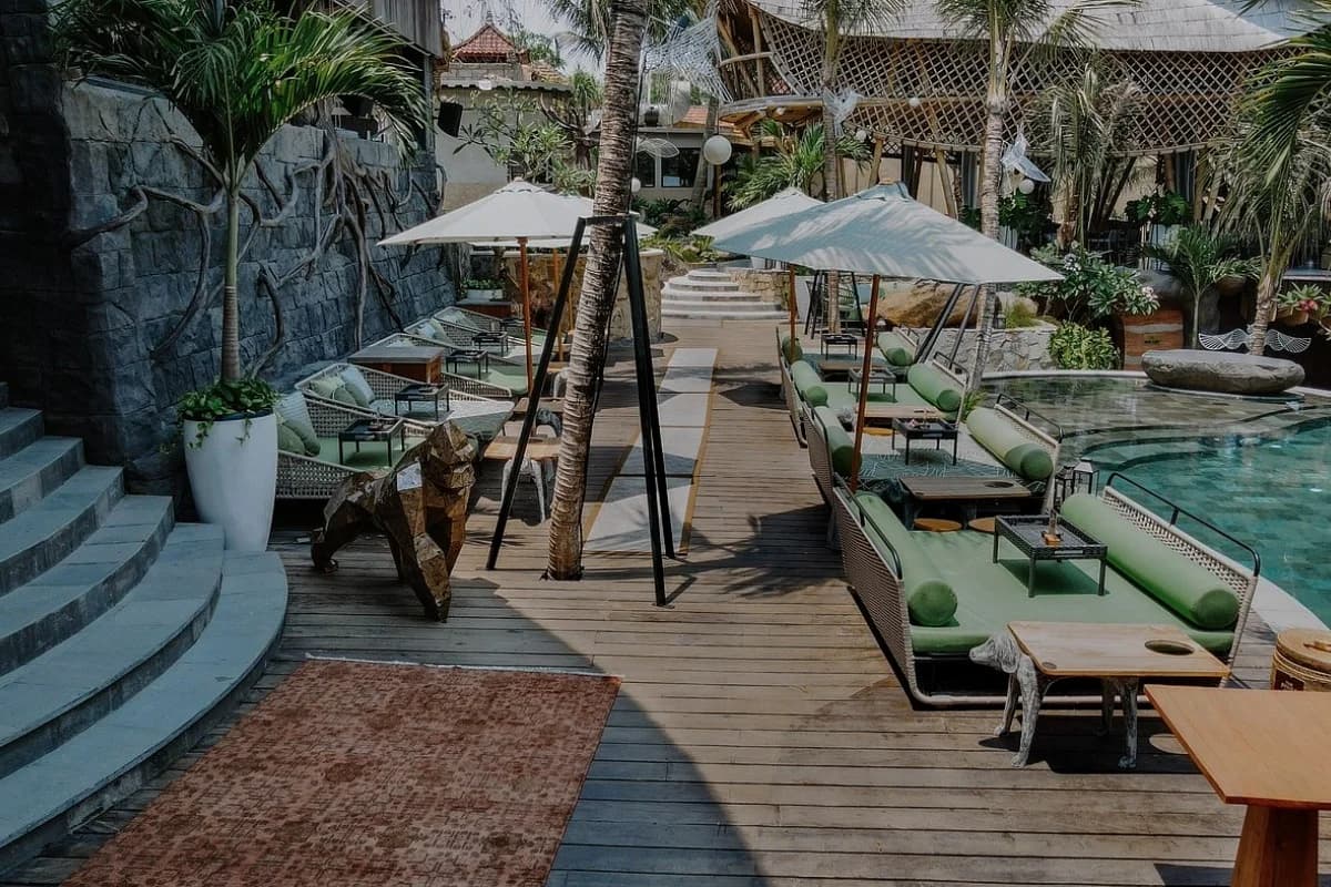 Bali day club with poolside seating, umbrellas, wooden deck, tropical plants, and a relaxed outdoor dining area.