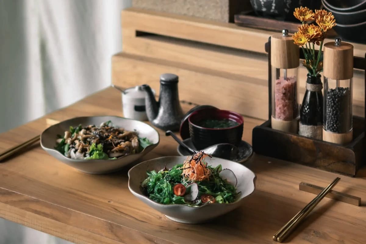 Japanese dishes, seaweed salad, soup, chopsticks, and condiments arranged on a wooden restaurant table.