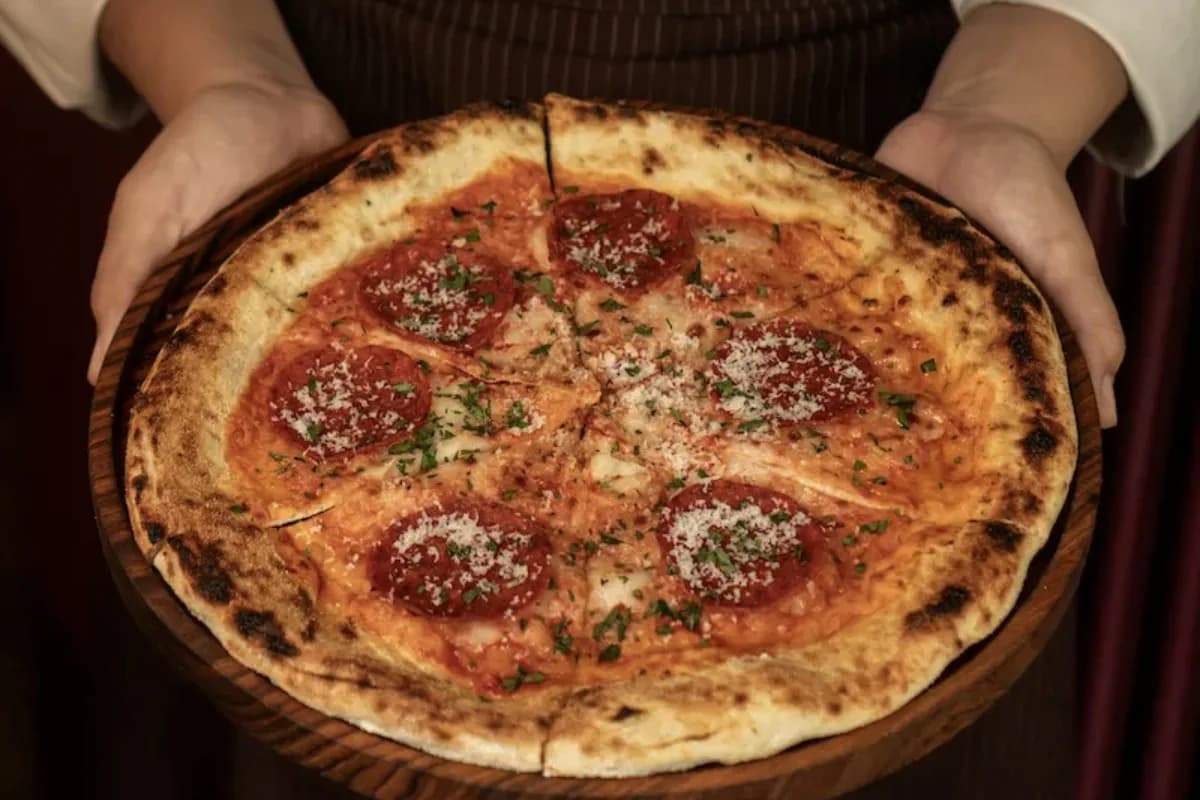 A freshly baked pepperoni pizza with a charred crust, tomato sauce, cheese, herbs, and sliced pepperoni.