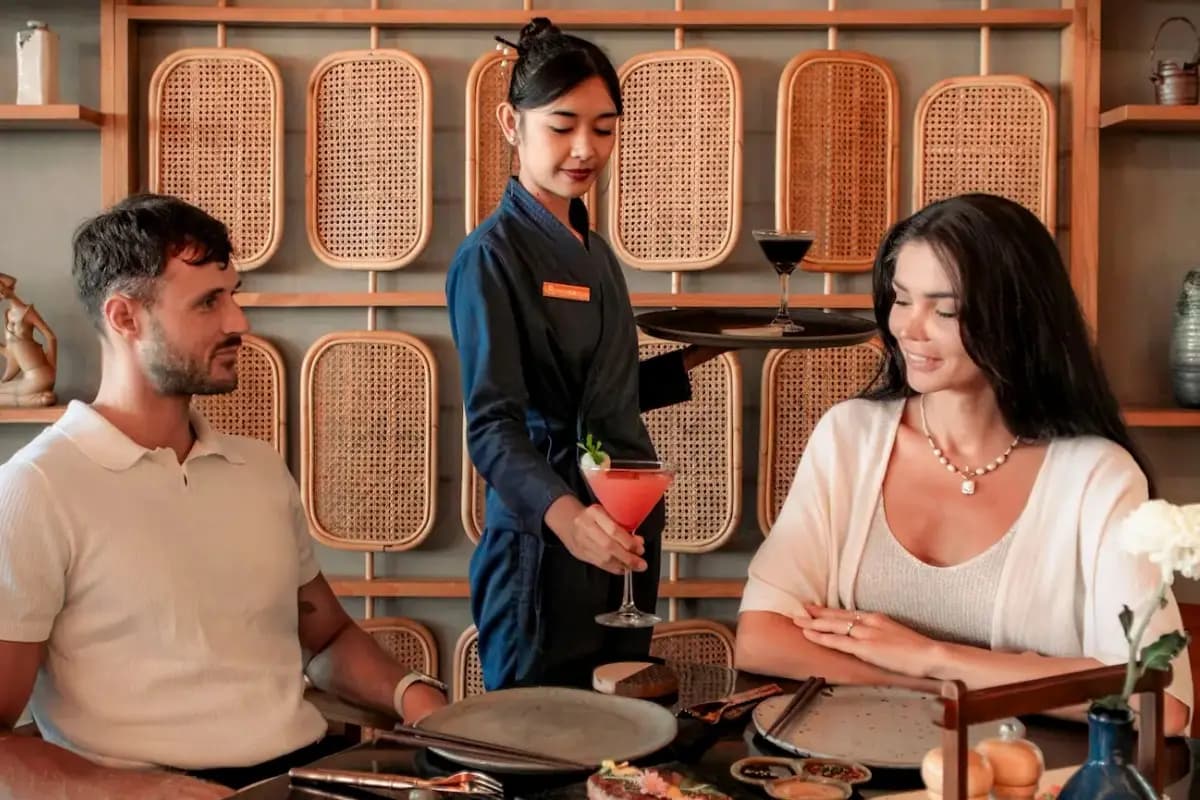 Pelayan menyajikan cocktail kepada pasangan di restoran, suasana makan malam romantis di Bali.