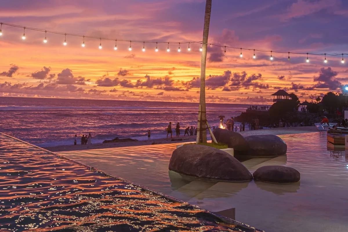Beach club in Bali with sunset ocean views, infinity pool, and evening lights by the shoreline.