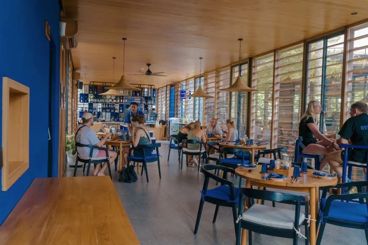 Bright Bali restaurant with diners enjoying brunch at tables beside large windows and an open bar.