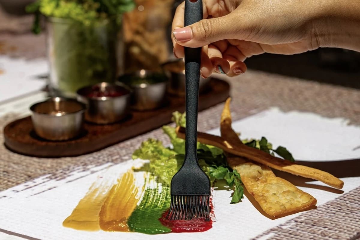 A chef uses a brush to arrange colorful sauces beside crisp bites for a Bali tasting menu.