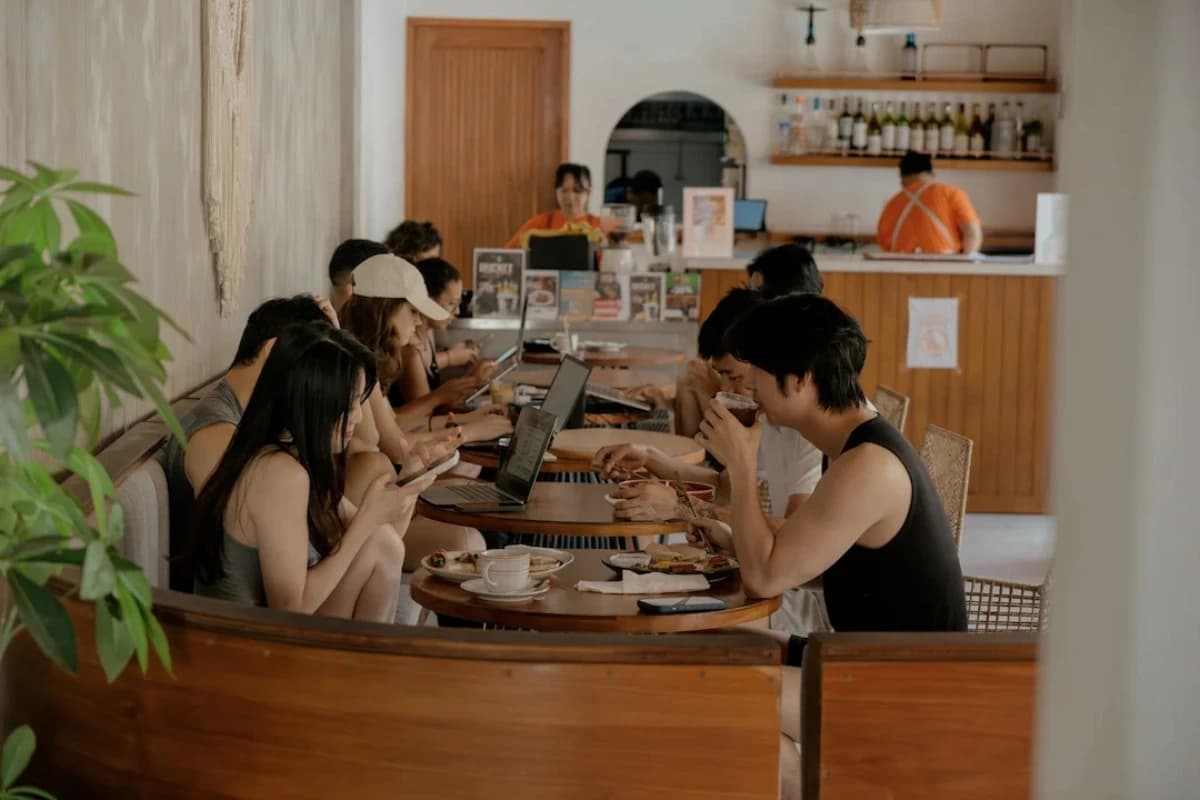 People work on laptops and enjoy drinks and meals at shared wooden tables inside a cafe in Canggu.