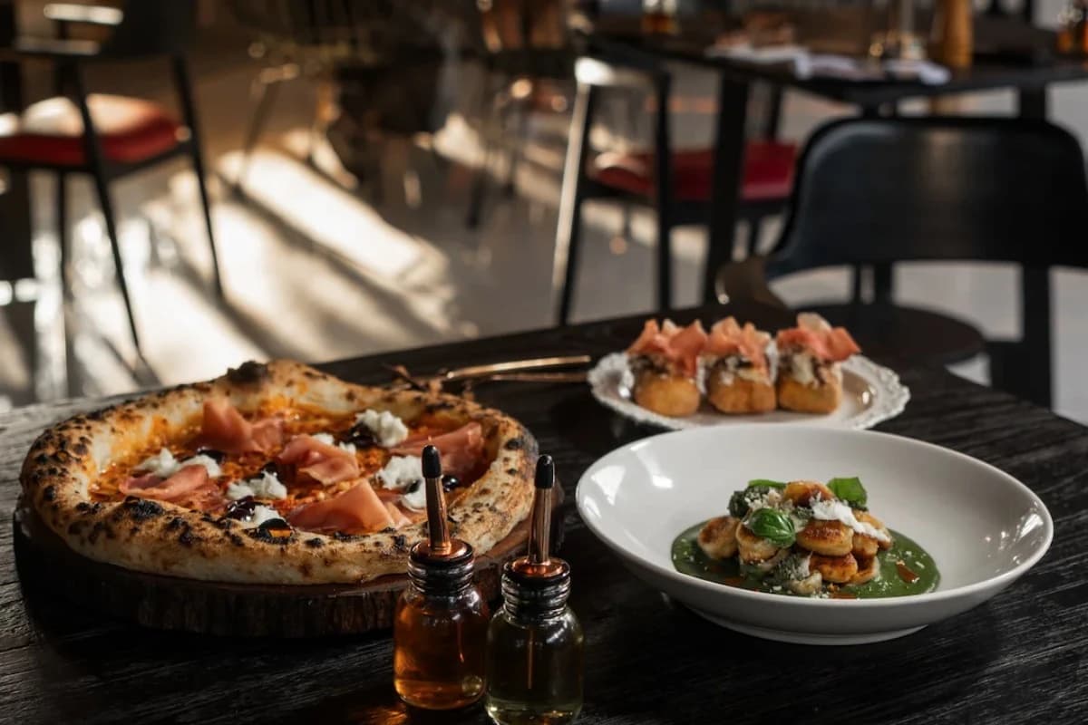 Wood-fired pizza, gnocchi with green sauce, and Italian appetizers served on a dark wooden table at a restaurant in Seminyak.