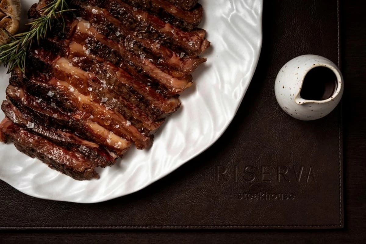 Sliced grilled steak with rosemary and sea salt served on a white plate beside sauce at Riserva Steakhouse in Bali.